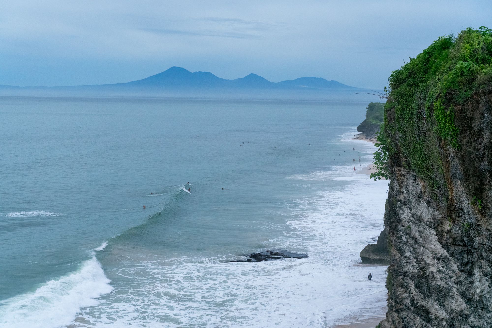 The Uluwatu cliffs above the surf at dusk, the volcanoes of the mainland on the horizon.