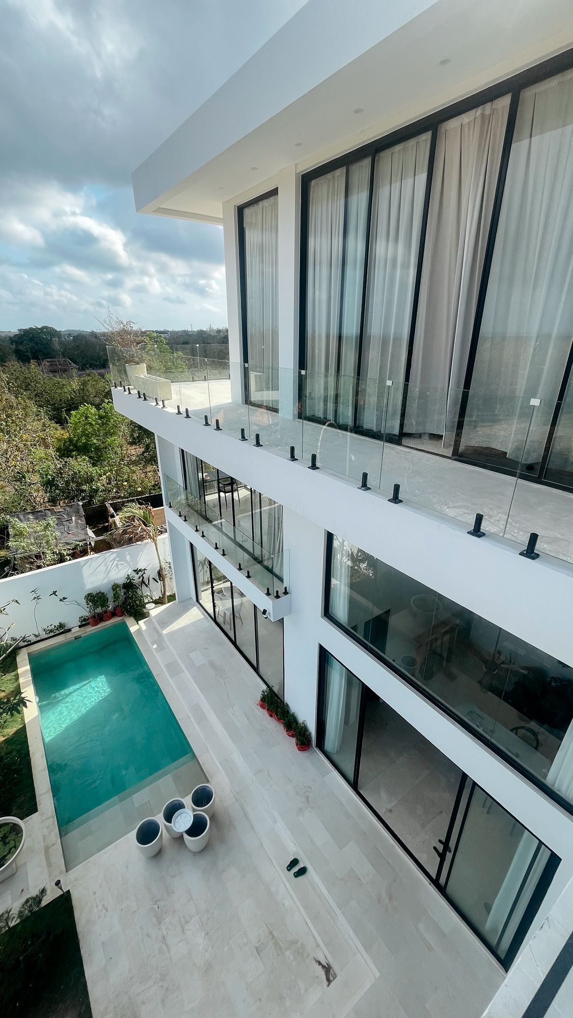 The white villa from the garden — stacked volumes, black-glass sliders and the pool below.