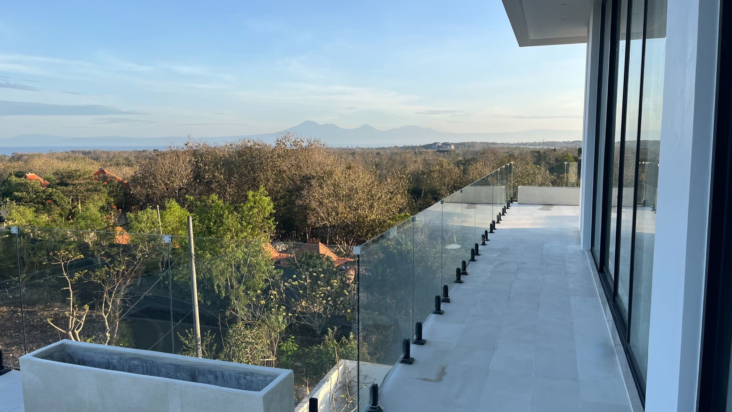 The master bedroom terrace behind a glass rail, the Bukit falling away to the sea and the volcanoes on the far horizon.